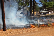 Firefighters and other emergency officials work to put out a grass fire on Corvette Lane in Queen City on Monday.